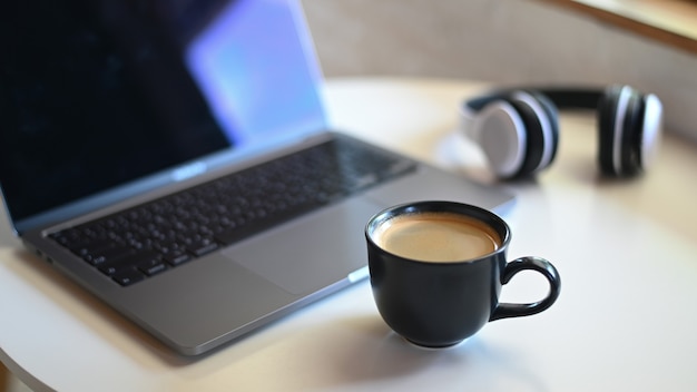 Zdjęcie zbliżenie kubek kawy z niewyraźne laptopa i słuchawek na umieszczone na stole w kawiarni.