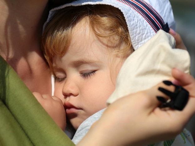 Zdjęcie zbliżenie ładny piękny beztroski niewinny chłopiec głęboko śpiący na rękach matki słoneczny dzień outd