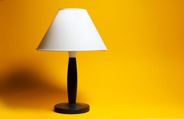 Zbliżenie: lampka nocna z białym abażurem i czarnym statywem na tle koloru pomarańczowego.