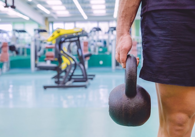 Zbliżenie lekkoatletycznego mężczyzna trzyma czarny żelaza Kettlebell w treningu crossfit na centrum fitness