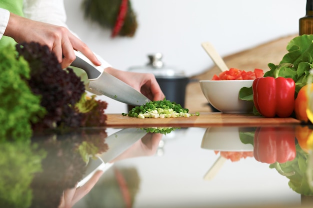 Zbliżenie ludzkich rąk gotowanie sałatka warzywna w kuchni na szklanym stole z odbicia. Zdrowy posiłek i koncepcja wegetariańska