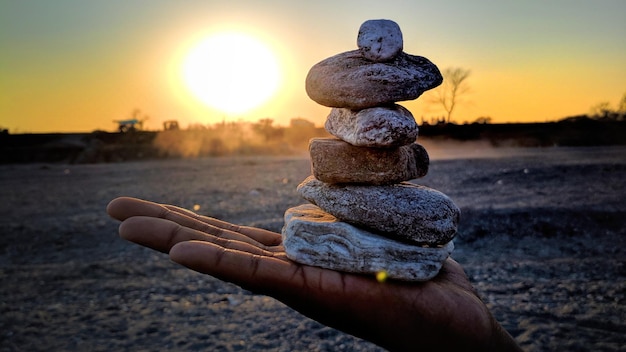 Zdjęcie zbliżenie ludzkiej ręki trzymającej ułożone kamienie podczas zachodu słońca