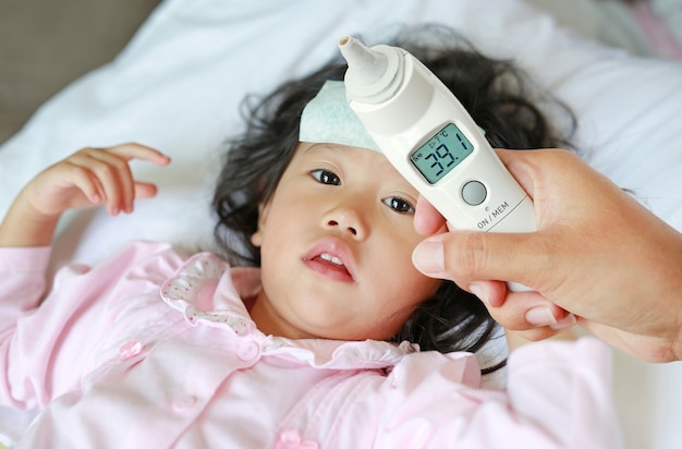 Zbliżenie Macierzysta Ręka Bierze Temperaturę Dla Jej Córki Z Uszatym Termometrem Na łóżku