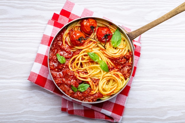 Zbliżenie: Makaron Spaghetti Z Mięsem I Sosem Bolońskim Pomidorowym Na Patelni Z Bazylią I Pomidorkami Cherry Na Białym Drewnianym Tle Rustykalnym, Widok Z Góry. Tradycyjna Włoska Kolacja