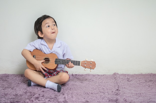 Zbliżenie małe dziecko w studenckim mundurze bawić się ukulele na dywanie z kopii przestrzenią