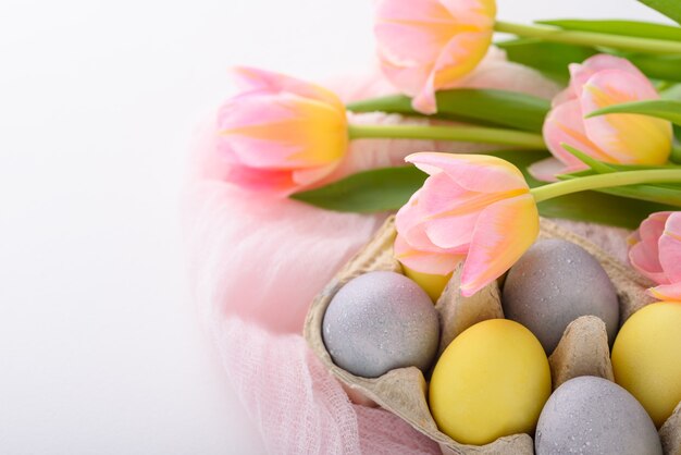 Zbliżenie malowane pisanki w pastelowy niebieski i żółty w tekturowym pudełku z różowe tulipany na białym tle