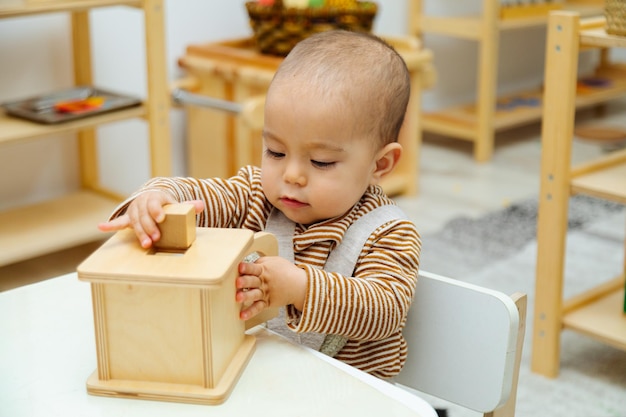 Zbliżenie malucha bawiącego się kwadratowym pudełkiem montessori