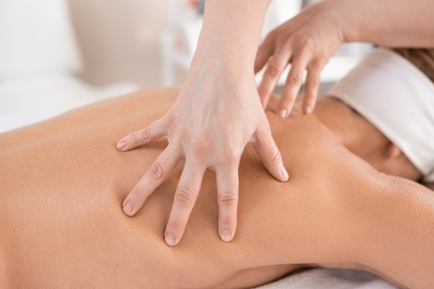 Zbliżenie: masażysta rozpieszczający mięśnie pleców kobiety podczas wykonywania masażu ręcznego w salonie spa