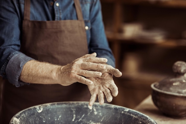 Zbliżenie męskich rąk garncarza, biorąc glinę z miski