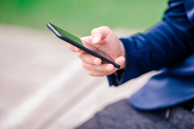 Zbliżenie męskie ręki trzyma telefon komórkowego outdoors na ulicie. Człowiek za pomocą smartfona.