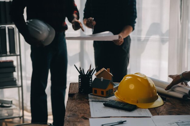 Zdjęcie zbliżenie męskiego inżyniera budowlanego z azji pracującego nad projektem architektonicznym na placu budowy przy biurku w biurze