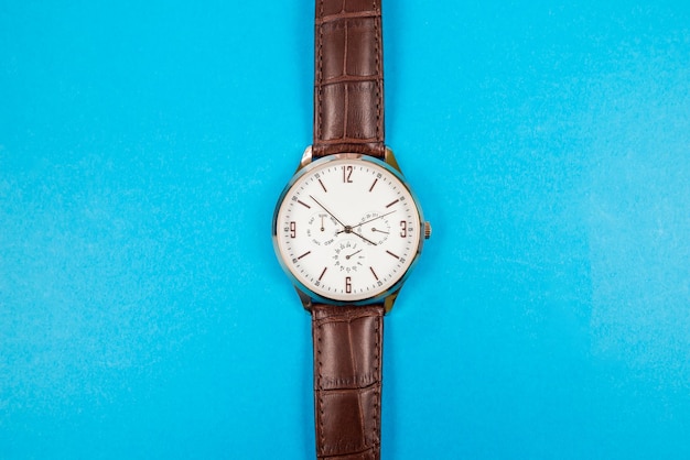 Zbliżenie męskiego zegarka na rękę wyizolowanego na niebieskim tle Męski zegarek na rękę z brązowym skórzanym paskiem