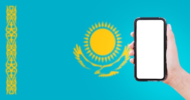 Zbliżenie męskiej ręki trzymającej smartfon z pustym ekranem na tle niewyraźne flaga Kazachstanu