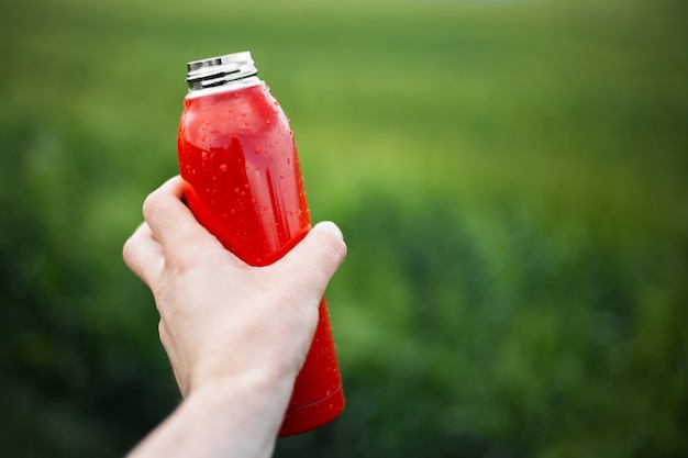 Zbliżenie: męskiej ręki trzymającej stalową butelkę termiczną wielokrotnego użytku w kolorze czerwonym spryskane wodą