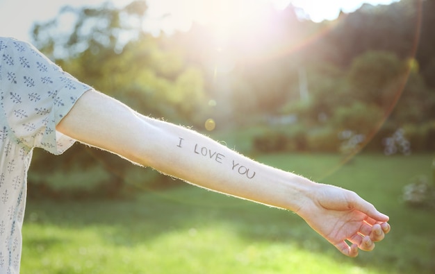 Zbliżenie męskiej ręki z tekstem „Kocham cię” napisanym na skórze na słonecznym tle przyrody