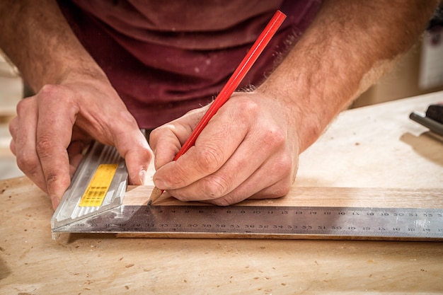 Zbliżenie Mężczyzna mierzy drewnianą deskę linijką i zaznacza ołówkiem niezbędne punkty na plastry