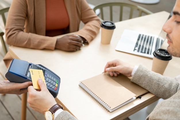 Zbliżenie: mężczyzna płaci za kawę kartą kredytową podczas spotkania ze swoim partnerem w kawiarni