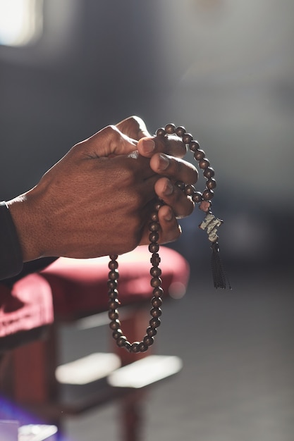 Zbliżenie: mężczyzna trzymający różaniec modlący się podczas wizyty w kościele