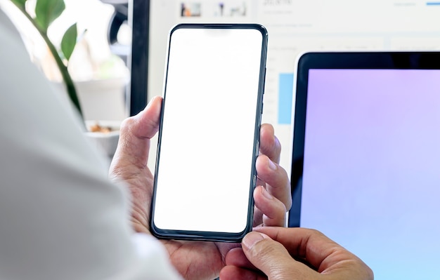 Zbliżenie mężczyzna używa smartphone z pustym ekranem podczas gdy siedzący przy biurowym biurkiem.