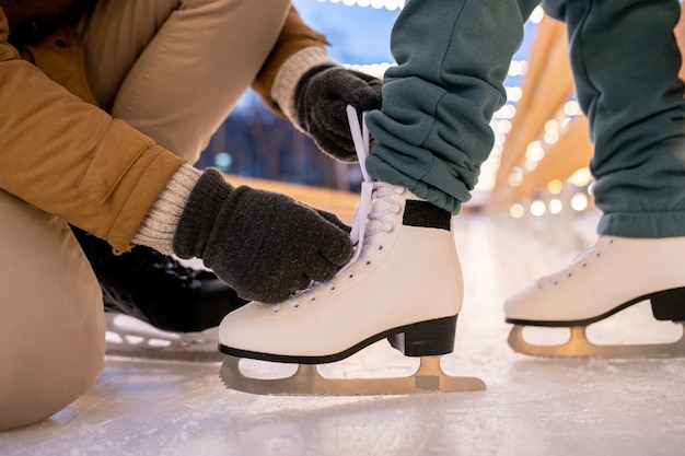 Zbliżenie: mężczyzna zawiązujący sznurowadła na łyżwach swojej dziewczyny, gdy stoją na lodowisku