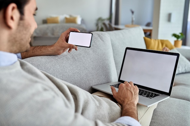 Zbliżenie mężczyzny korzystającego z laptopa i telefonu komórkowego podczas relaksu w salonie