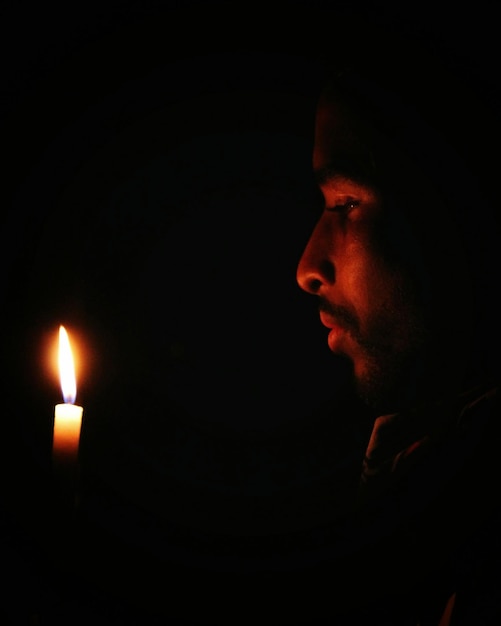 Zdjęcie zbliżenie mężczyzny patrzącego na płonącą świecę w ciemni