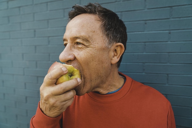 Zbliżenie mężczyzny w średnim wieku jedzącego słodkie jabłko na niebieskim tle
