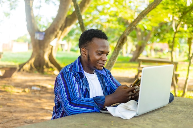 Zbliżenie młodego afrykańskiego studenta kampusu za pomocą telefonu komórkowego i laptopa w środowisku szkolnym