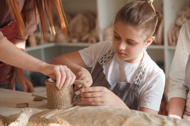 Zbliżenie młodego chłopca robi kubek ceramiczny z pomocą profesjonalnego garncarza w studiu artystycznym