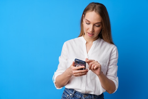 Zbliżenie młodej blondynki za pomocą smartfona na niebieskim tle