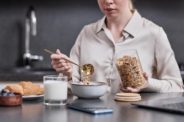 Zbliżenie młodej kobiety cieszącej się zdrowym śniadaniem rano wylewania muesli w misce ze złotym spo