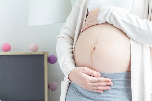 Zdjęcie zbliżenie młodej kobiety w ciąży trzymającej ręce na brzuchu w ostatnim trymestrze ciąży koncepcja kochania ciąży