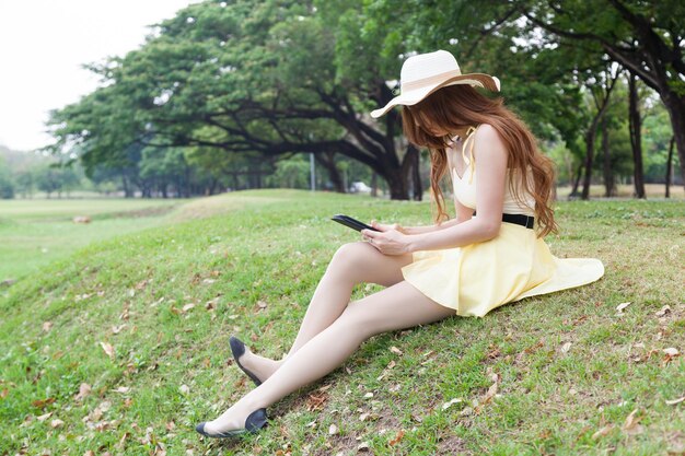 Zbliżenie młodej kobiety z cyfrowym tabletem siedzącej na trawiastym polu