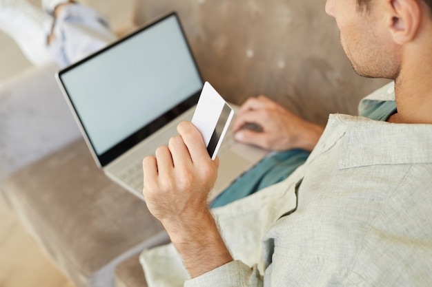 Zbliżenie: młody człowiek posiadający kartę kredytową i płacenie online za zakupy przy użyciu komputera przenośnego