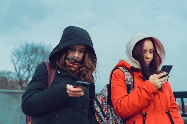 Zbliżenie młodych kobiet przeglądających smartfon w parku miejskim Ładne kobiety w kapturach za pomocą telefonu komórkowego