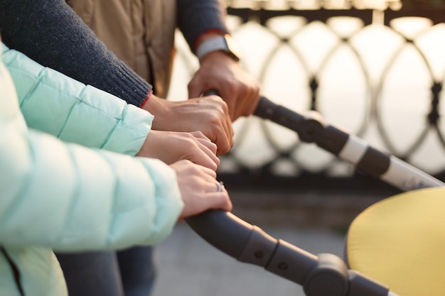 Zbliżenie młodych kochających rodzinnych rąk trzymających wózek nad jeziorem rodziców z wózkiem jesienią