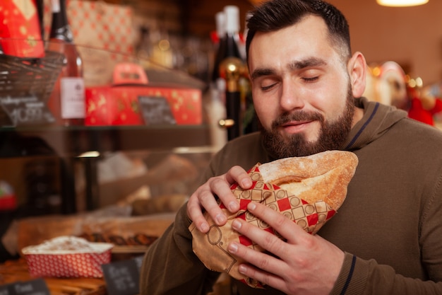 Zbliżenie na brodatego mężczyznę uśmiechniętego z zamkniętymi oczami, zapachu pysznego świeżego chleba w piekarni