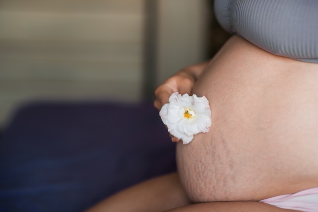 Zbliżenie Na Brzuch Kobiety W Ciąży Z Delikatnym Pięknym Kwiatem. Naturalna Tekstura Skóry Kobiety W Ciąży