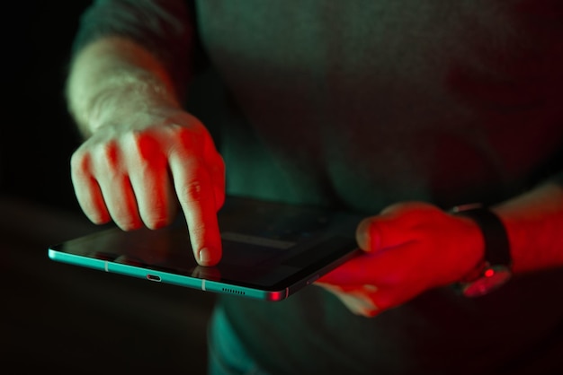 Zdjęcie zbliżenie na ciemne zdjęcie mężczyzny dotykającego ekranu cyfrowego tabletu w czerwonym świetle