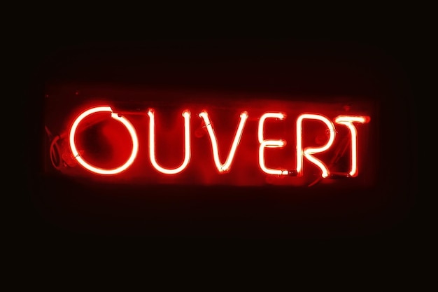 Zdjęcie zbliżenie na czerwonym świetle neonu w kształcie francuskiego słowa ouvert oznaczającego w języku angielskim „otwarty”.