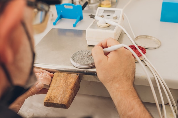 Zbliżenie Na Dorosłego Mężczyznę Rasy Kaukaskiej, Który Używa Wosku Do Formowania Pleśni Dentystycznej, Siedząc W Laboratorium Specjalizującym Się W Ceramice Kości Dentystycznej Do Tworzenia Koron Porcelanowych.