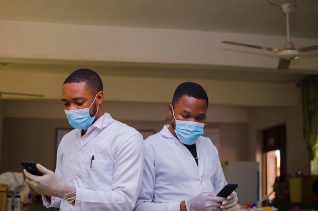 Zdjęcie zbliżenie na dwóch afrykańskich lekarzy w laboratorium obsługujących telefon