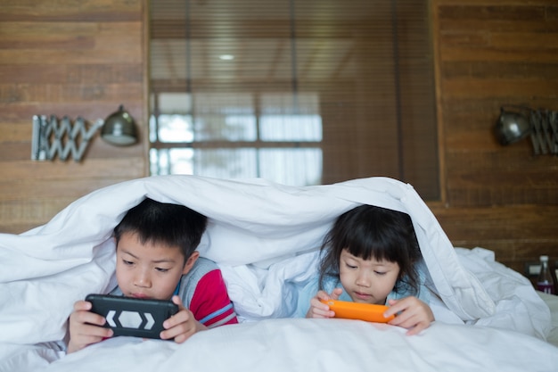 Zbliżenie na dzieci grające na telefonach w łóżku