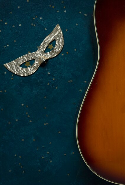 Zbliżenie na gitarę akustyczną i karnawałową maskę na niebieskim tle z brokatem