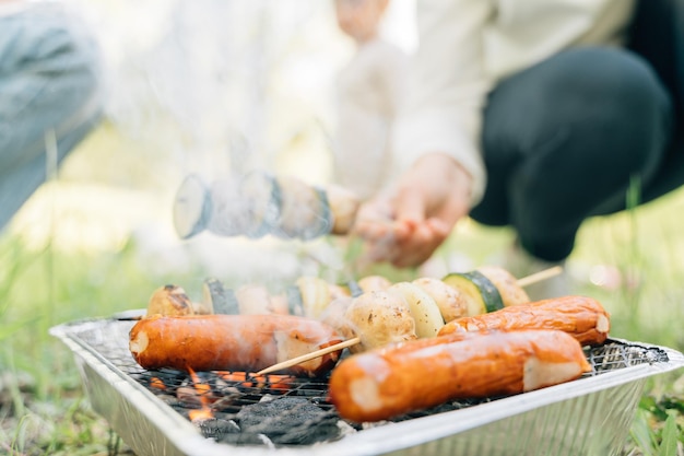 Zbliżenie na grill jednorazowego użytku na piknik na świeżym powietrzu z warzywami na drewnianym patyku