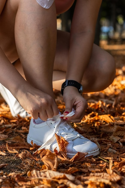 Zbliżenie na jedną sportsmenkę wiążącą sznurowadło na zewnątrz w publicznym parku jesienią