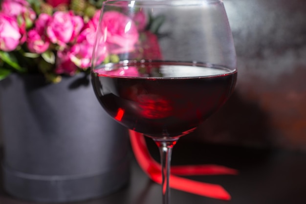 Zbliżenie na kieliszek z winem w pobliżu stylowego bukietu róż i czerwonych róż i czerwoną wstążką w okrągłym czarnym pudełku. Koncepcja walentynek i rocznicy