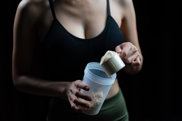 Zdjęcie zbliżenie na kobiety z miarką białka serwatki i butelką do wytrząsania, przygotowując shake proteinowy.