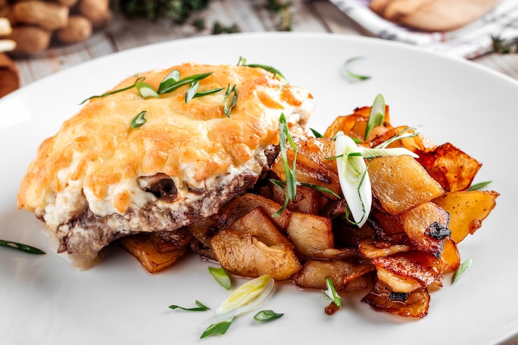 Zdjęcie zbliżenie na kotlet z sera z grilla z pieczonymi ziemniakami doprawionymi zieloną cebulą