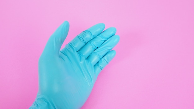 Zbliżenie na lewą rękę nosić rękawiczki lateksowe na różowym tle.